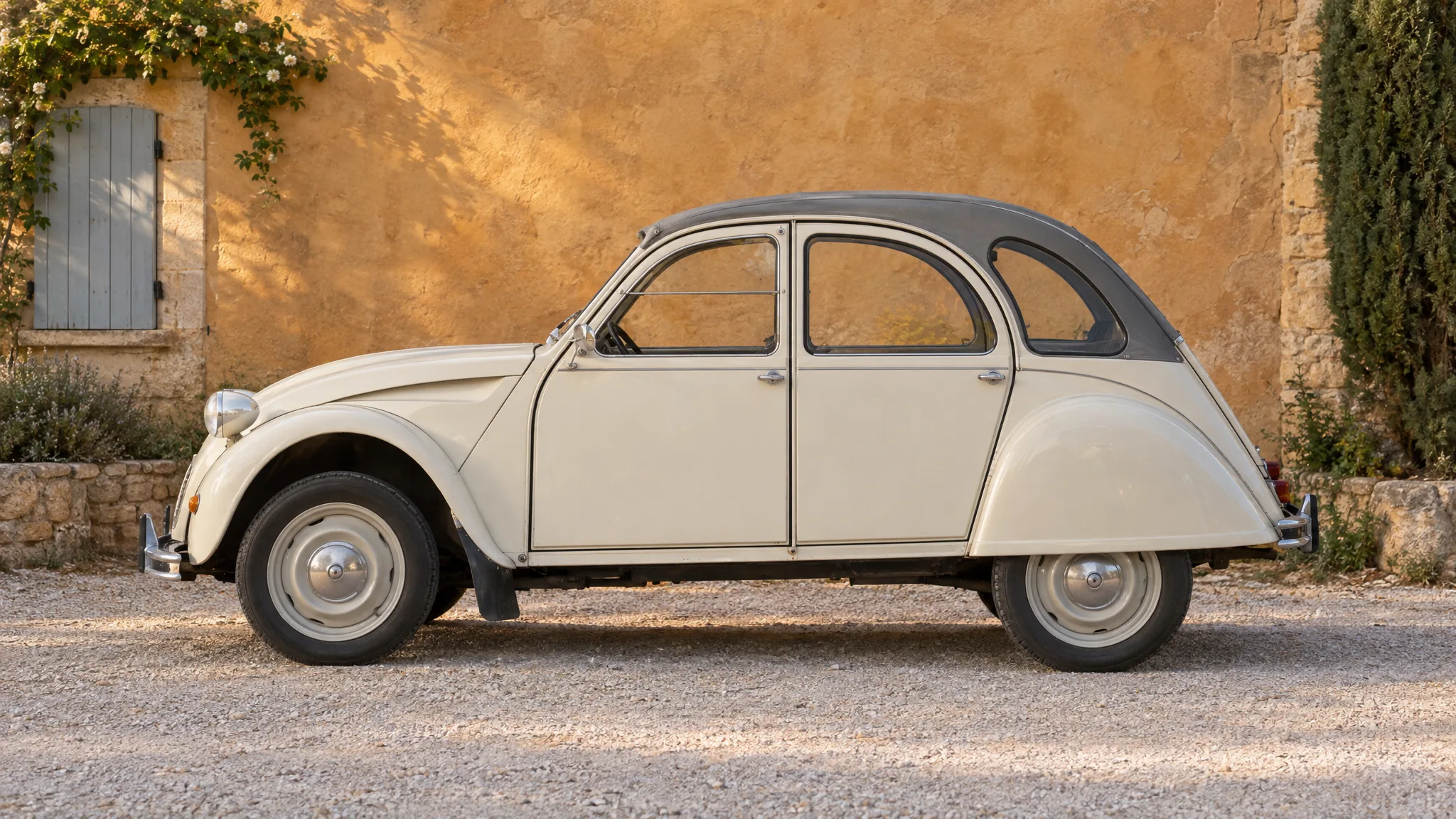 Een crèmewitte Citroën 2CV van opzij, voor een okergele muur in de Provence